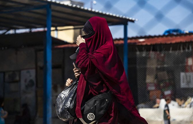 A woman hides walks past a fence at Camp Roj, where relatives of people suspected of belonging to the Daesh (IS) group are held, in the countryside near al-Malikiyah (Derik) in Syria's northeastern Hasakah province on October 8, 2023. (AFP/File)