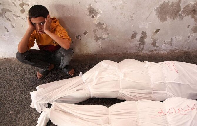 A Palestinian child sits next to the shrouded bodies of people killed in an Israeli strike. (AFP)