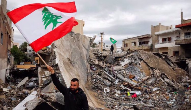 A man waves a Lebanese flag as he stands amidst the rubble of a building destroyed in Israeli strikes, after a ceasefire between Israel and Lebanon