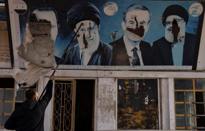 A worker tears down the pictures of Syria’s Bashar Assad, former Syrian President Hafez Assad, Lebanon’s late Hezbollah leader Hassan Nasrallah and Iran’s Supreme Leader Ayatollah Ali Khamenei at a gas station in Nubl, a Shiite village seized by militants, in rural Aleppo, Dec. 11, 2024. (Reuters)