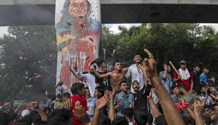 Protesters celebrate beside a defaced portrait of Prime Minister Sheikh Hasina after news of her resignation, in Dhaka, Bangladesh, on Aug. 5, 2024. (AP Photo/Fatima Tuj Johora File)
